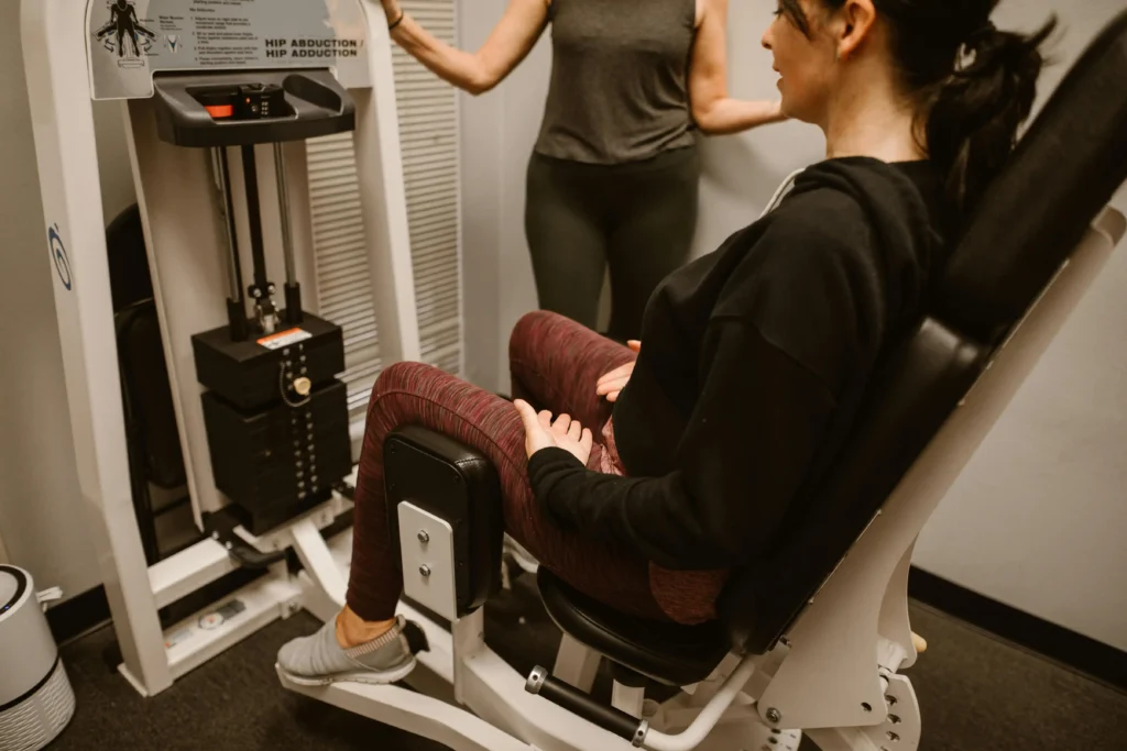 Female client using hip abduction machine under trainer guidance at Herburn Studio ladies-only fitness centre