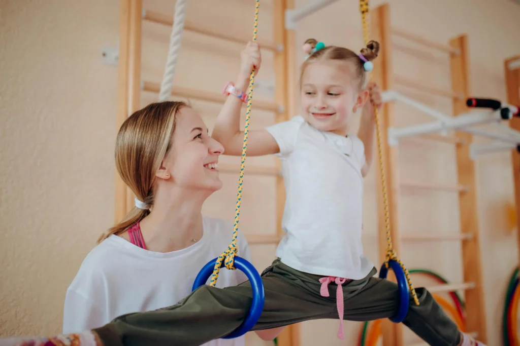 Mother helping daughter practice gymnastics on rings during kids fitness training